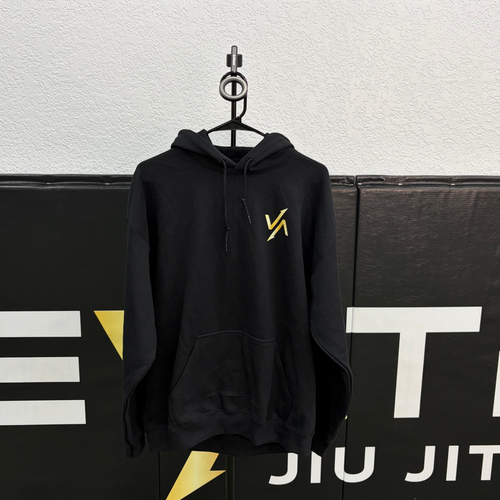 Black hoodie with a yellow logo on a hanger against a Brazilian and American flag background.